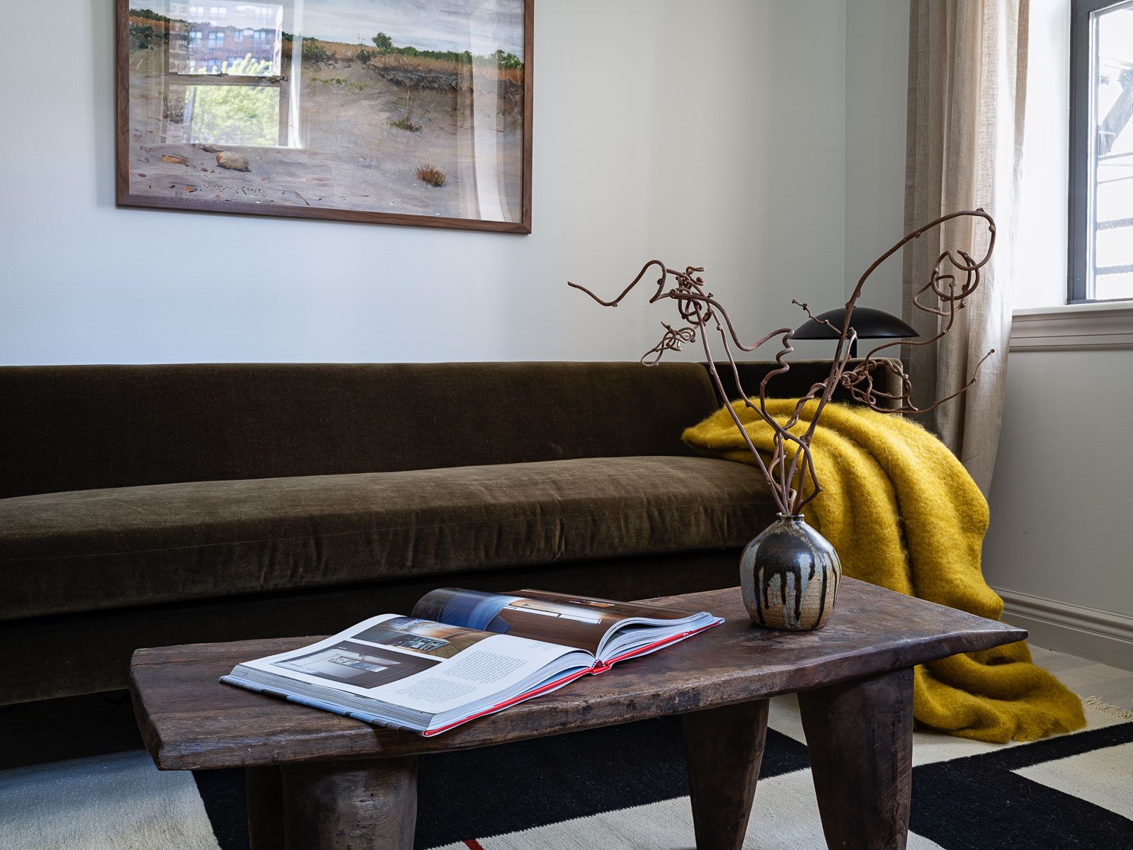Living room photo with a green long sofa, vintage coffee table styled with a vase and yellow throw blanket