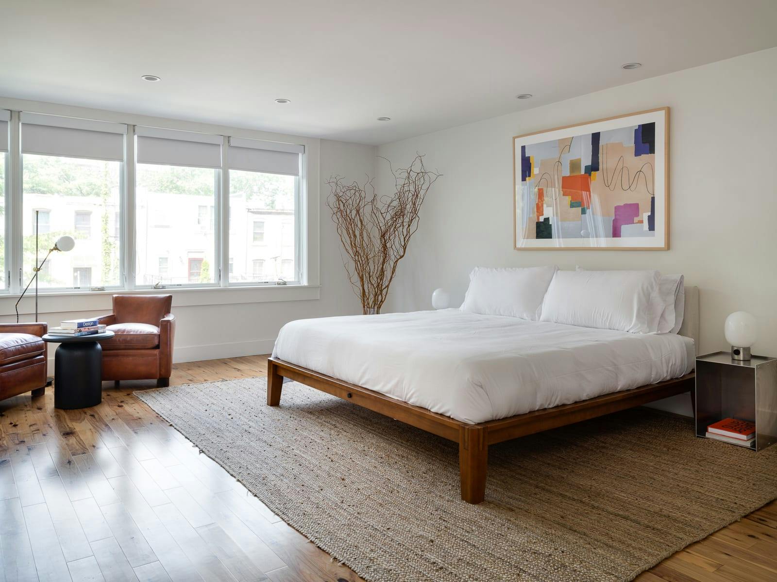 Large King Bedroom with Artwork, Dried Plants, Leather Arm Chairs and Side Table facing large windows and natural sunlight on jut rug