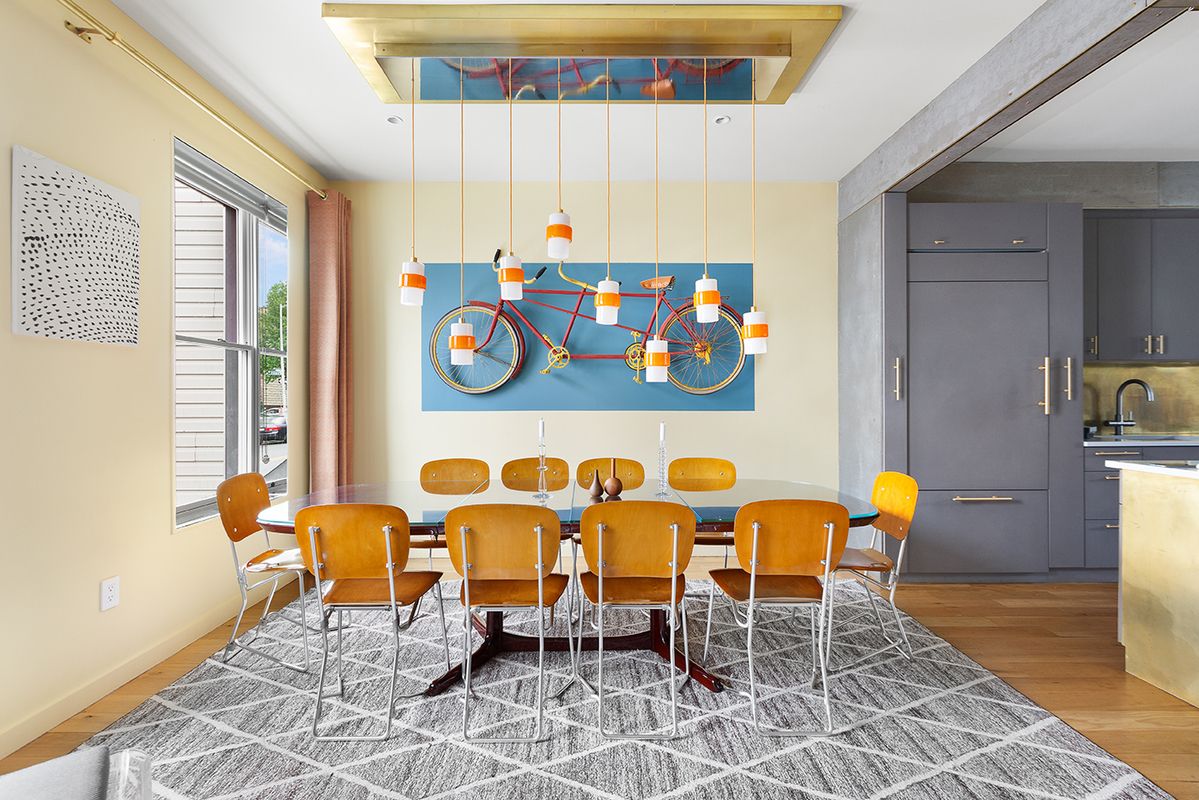 A dining room furnished with a table and chairs featuring a bike mounted on a wall and hanging lights in New York or Brooklyn furnished rental