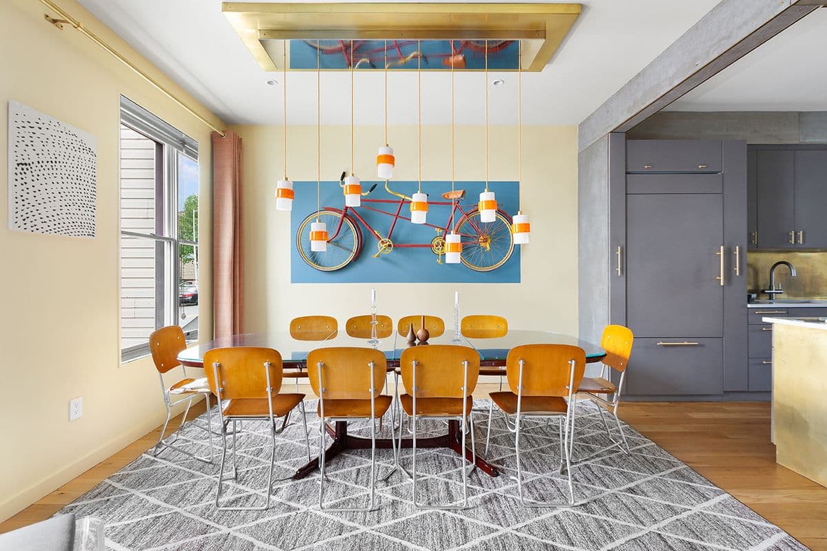 A dining room furnished with a table and chairs featuring a bike mounted on a wall and hanging lights in New York or Brooklyn furnished rental